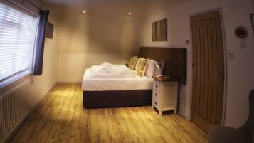 Een slaapkamer met een bed, nachtkastje, stoel en houten vloer.
