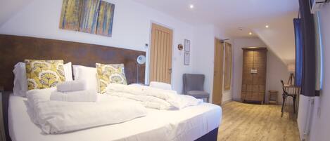 A well-lit bedroom with a large bed, a wooden wardrobe, and a chair.