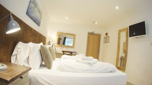 Quarto de hotel com cama, mesa de cabeceira, abajur, espelho, porta de madeira e televisão fixada na parede.