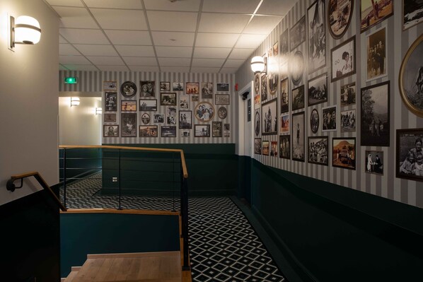 Un pasillo con piso estampado, una escalera y paredes decoradas con fotografías enmarcadas.