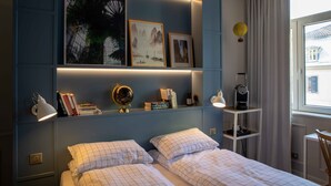 A bedroom with a bed, bedside tables, a shelf with books and a globe, and artwork on the wall.