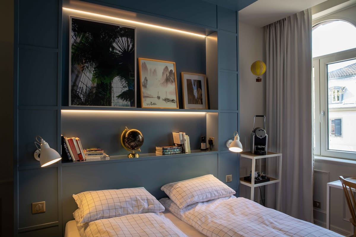 Un dormitorio con cama, mesitas de noche, una estantería con libros y un globo terráqueo, y una obra de arte en la pared.