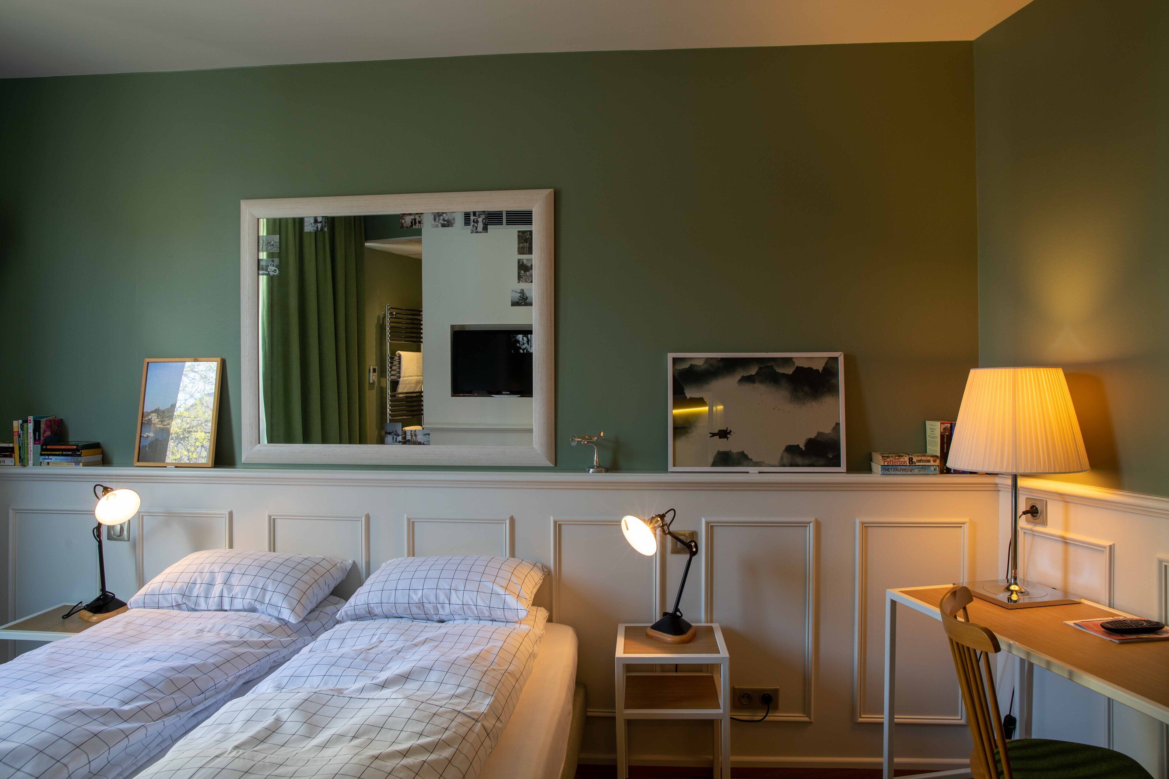 A bedroom with two beds, a desk, a chair, a mirror, and a lamp.