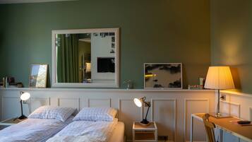 A bedroom with two beds, a desk, a chair, a mirror, and a lamp.