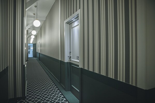 A hotel hallway with striped walls, a patterned floor, and doors numbered 12 and 13.