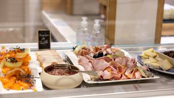 Buffet com diversos alimentos, incluindo carnes, queijos e frutas.