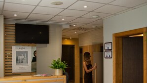 A reception area with a wooden reception desk, a potted plant, and a flat-screen TV mounted on the wall.