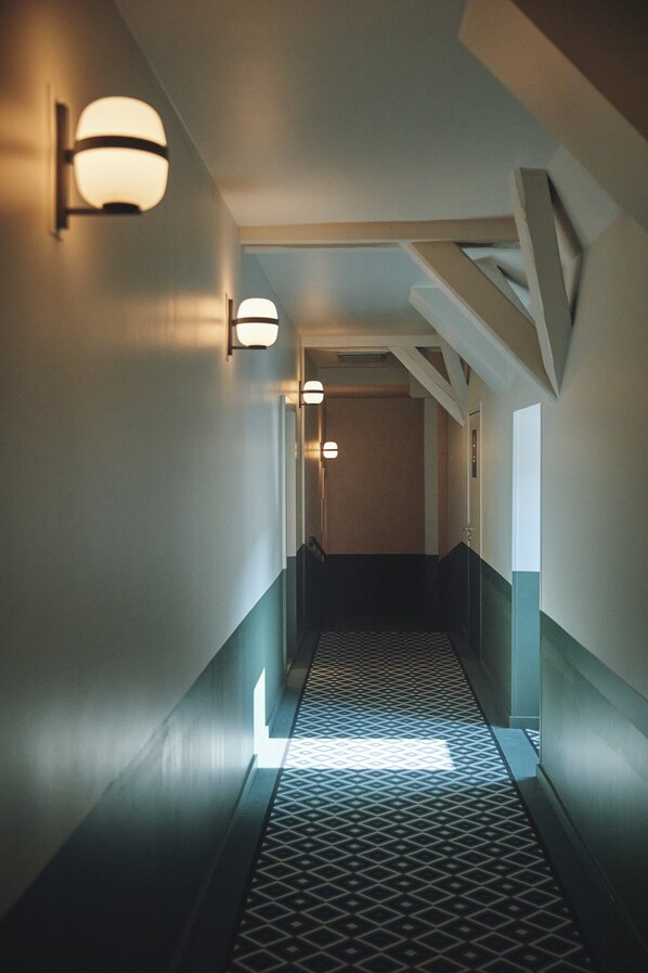 A hallway with patterned flooring, wall-mounted lights, and a door at the end.