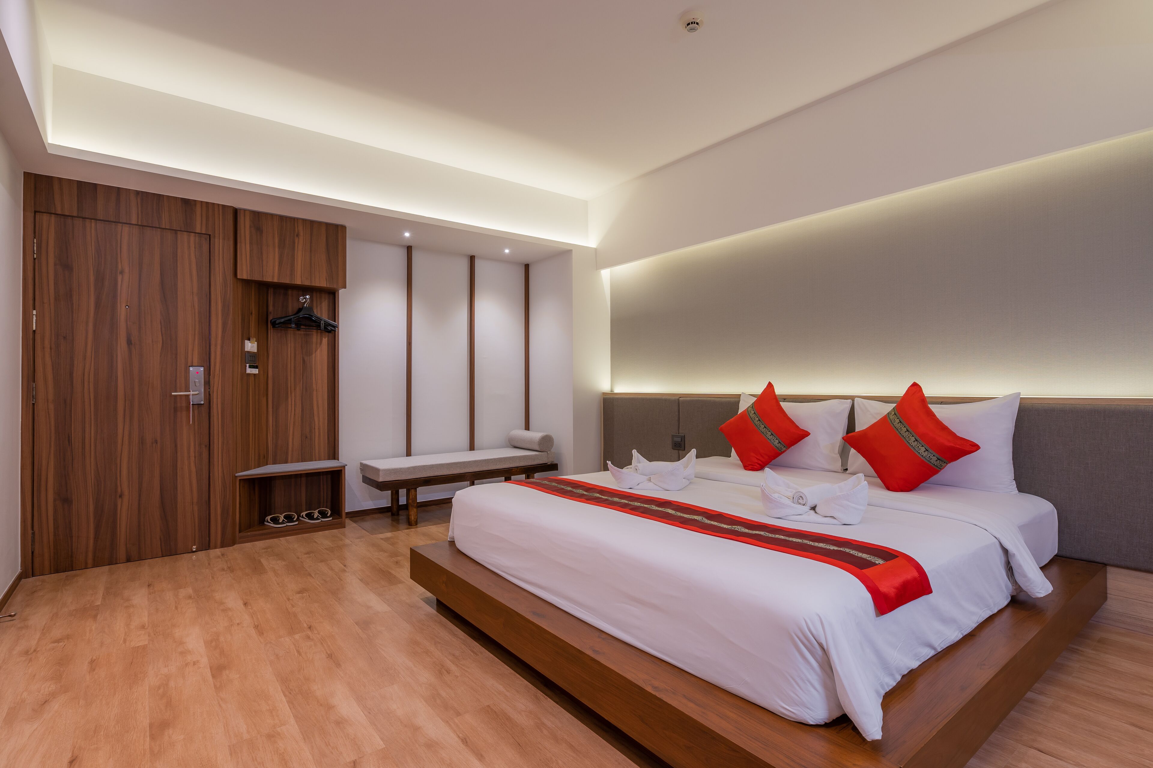 Ein modernes Hotelzimmer mit einem großen Bett, einem Holzschrank, einer eingebauten Bank und einem Nachttisch.
