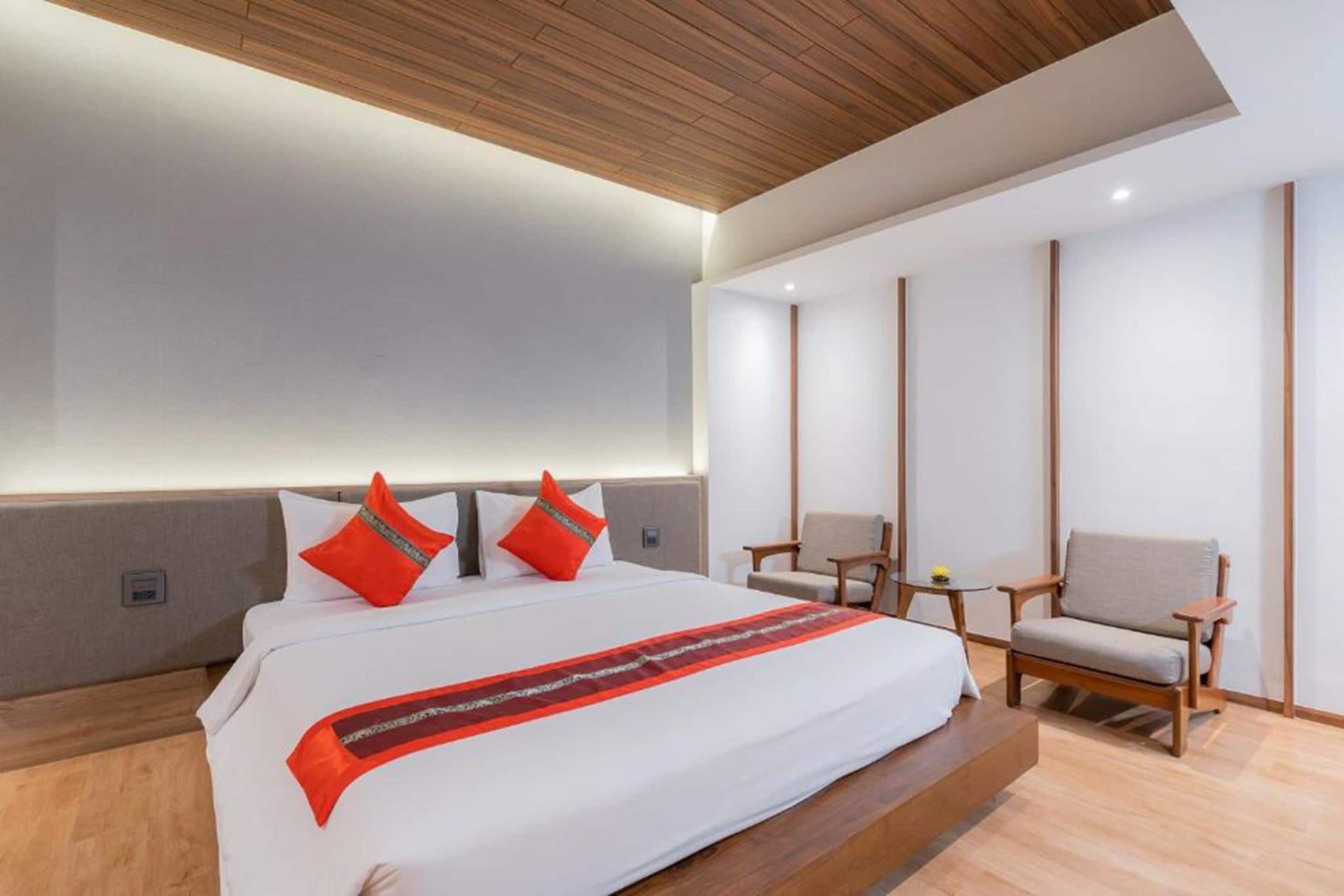 A modern hotel room with a large bed, two chairs, a small table, and a wooden ceiling.
