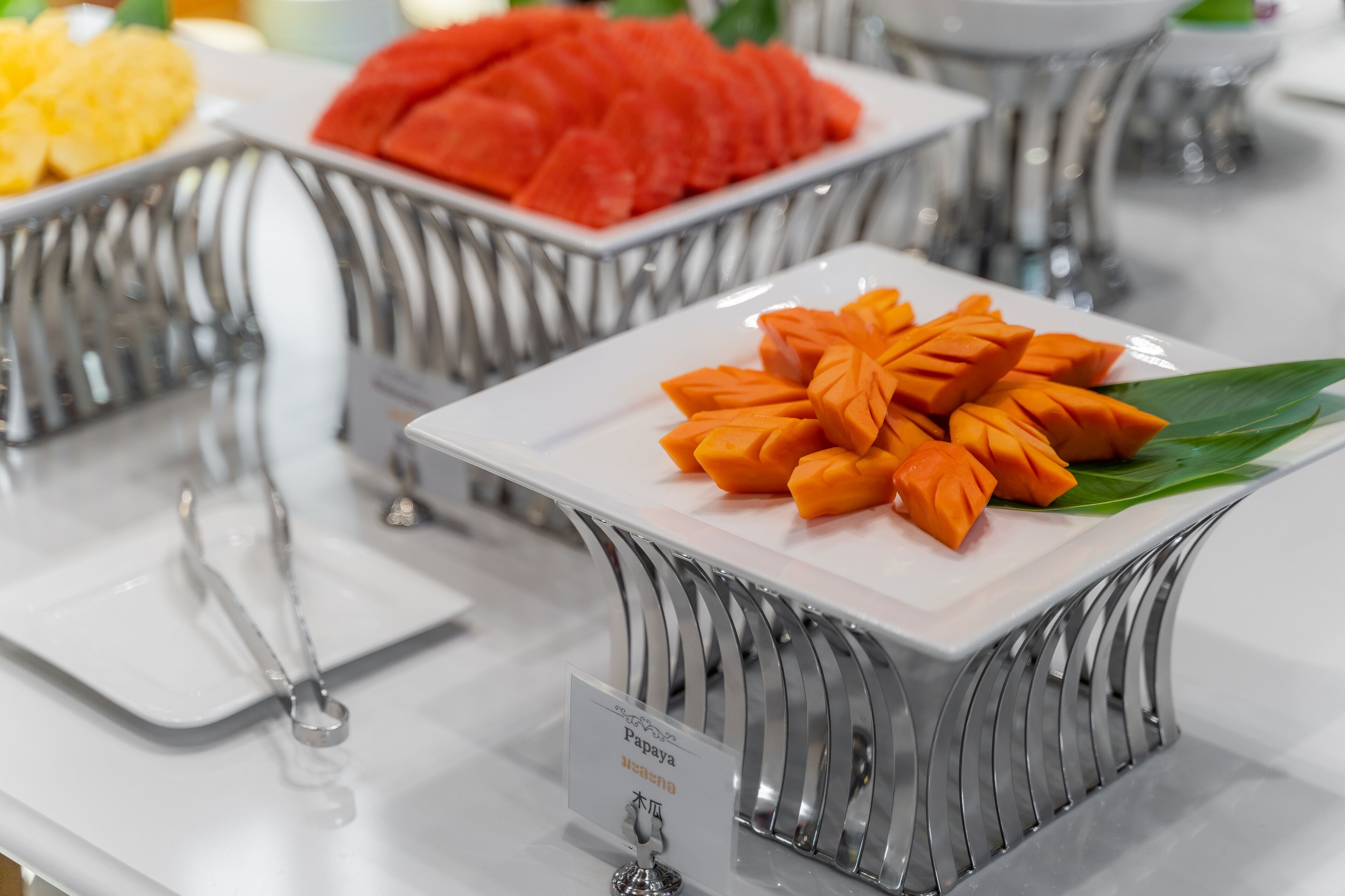 A buffet with various fruits and a sign indicating 'Papaya'.