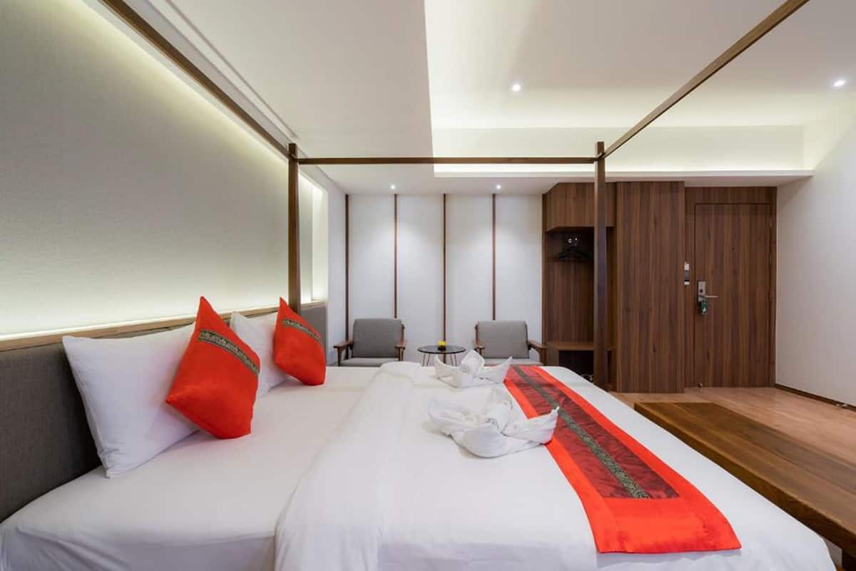 Una habitación de hotel moderna con una cama grande, dos sillones, una mesita pequeña y un armario de madera.