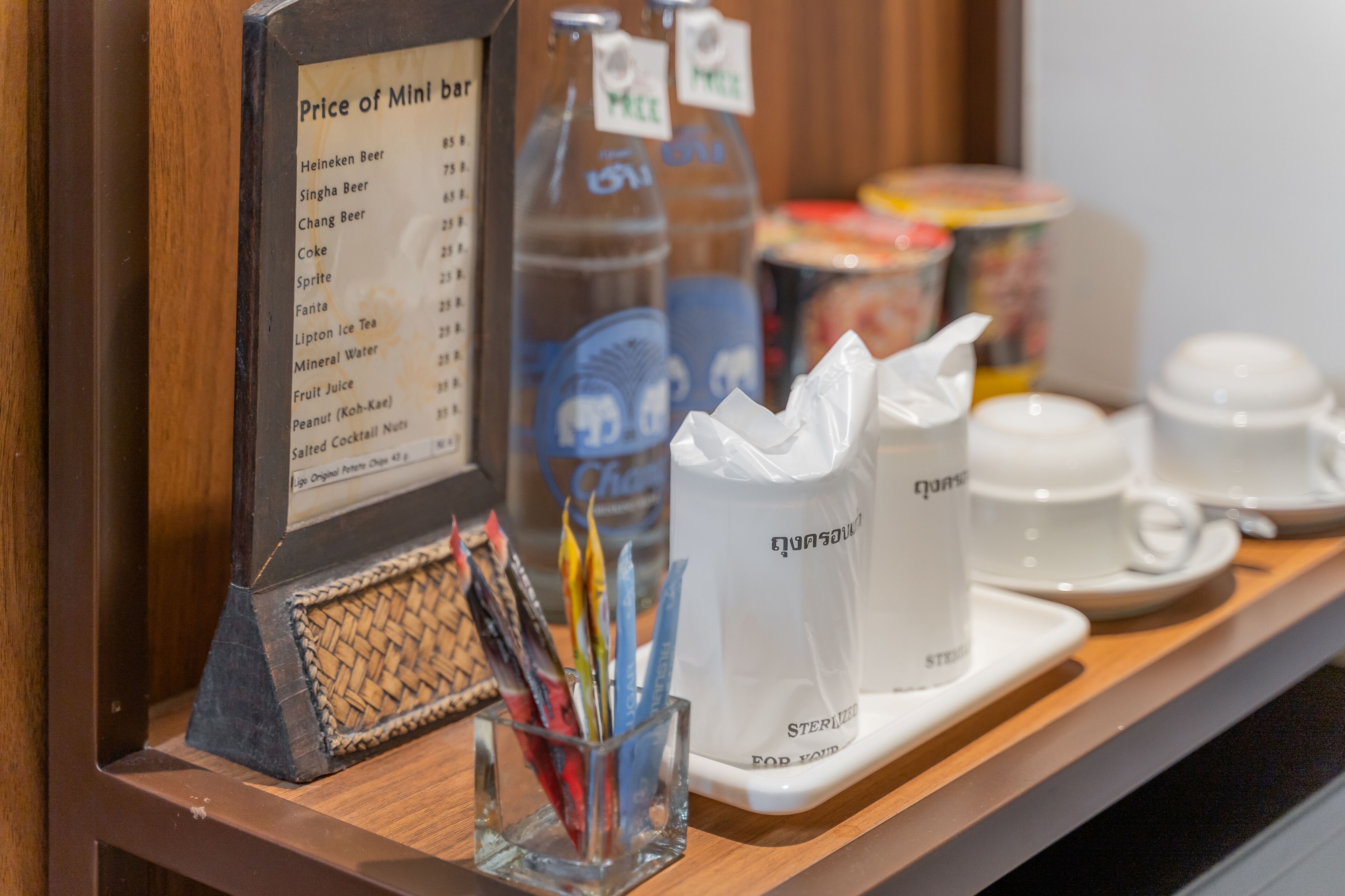 Mini bar com lista de preços, diversas bebidas e um pequeno recipiente com canetas.