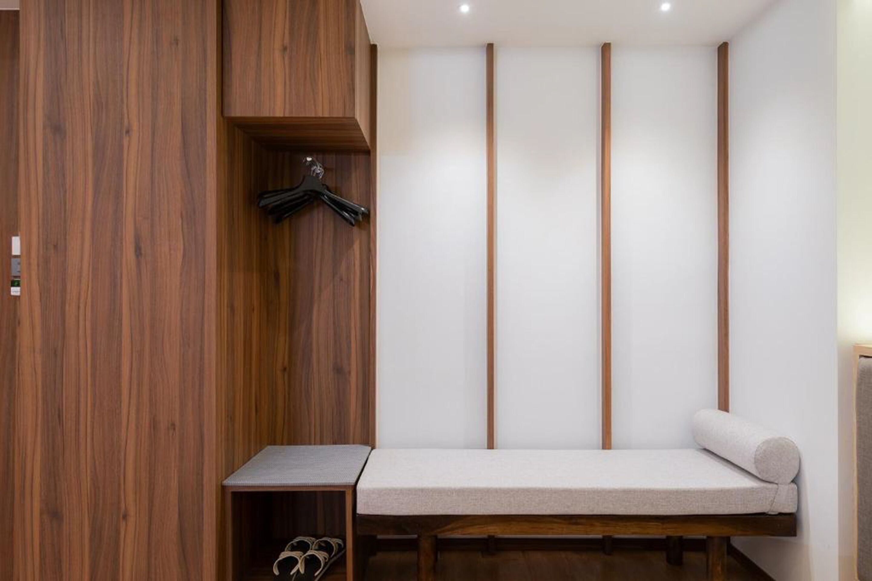 Een minimalistisch ingerichte kamer met een houten garderobe, een bankje met kussen en een schoenenrek.