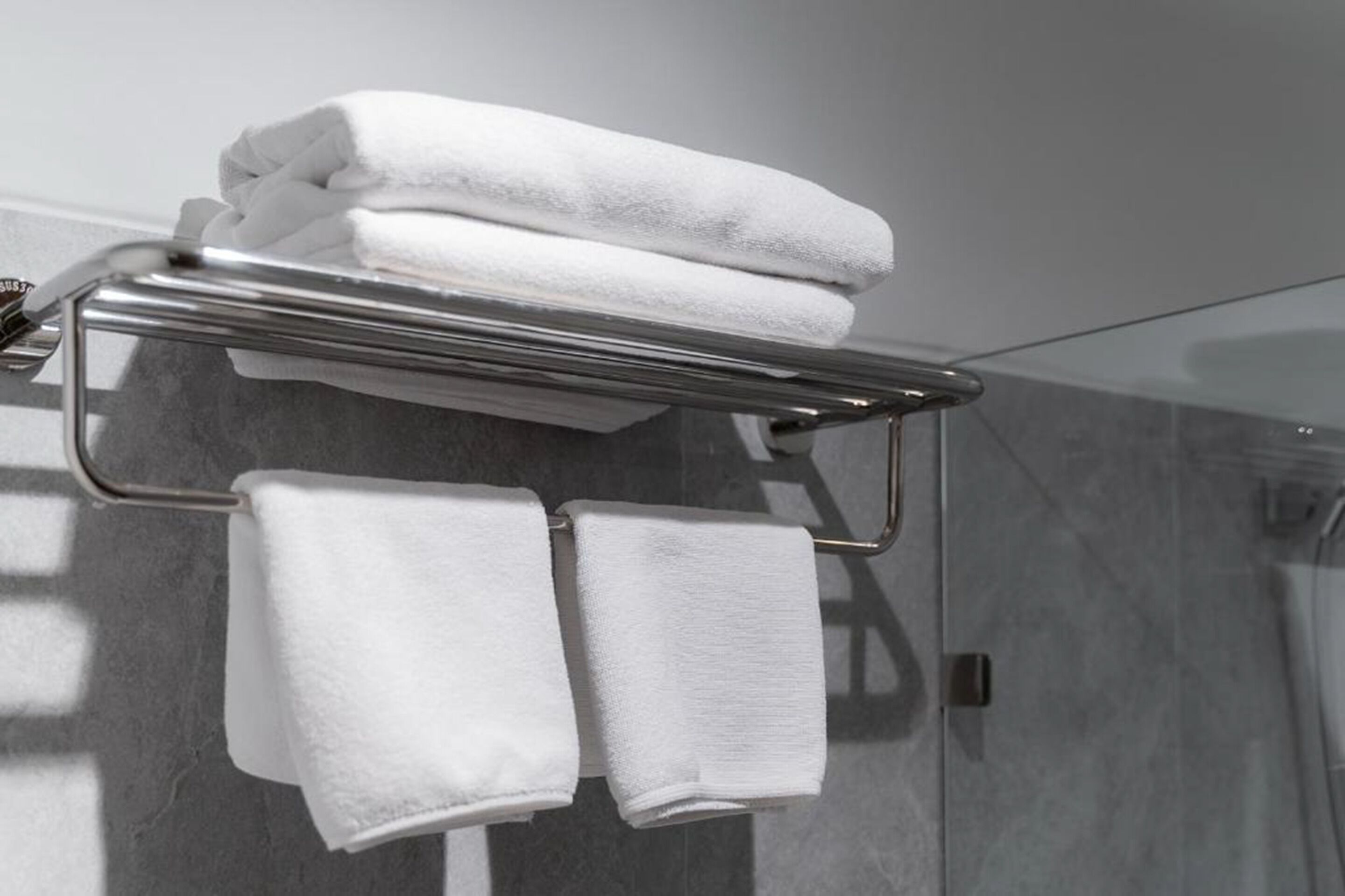A metal towel rack with two folded white towels hanging from it.
