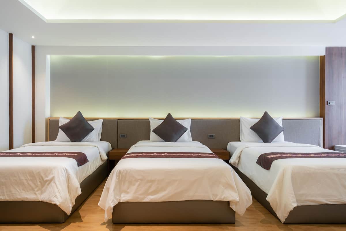 Habitación de hotel con tres camas dispuestas en fila, cada una con cabecera y almohadas.