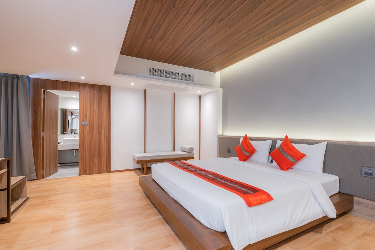 Una habitación de hotel moderna con una cama grande, piso de madera, un banco integrado y vista al baño.