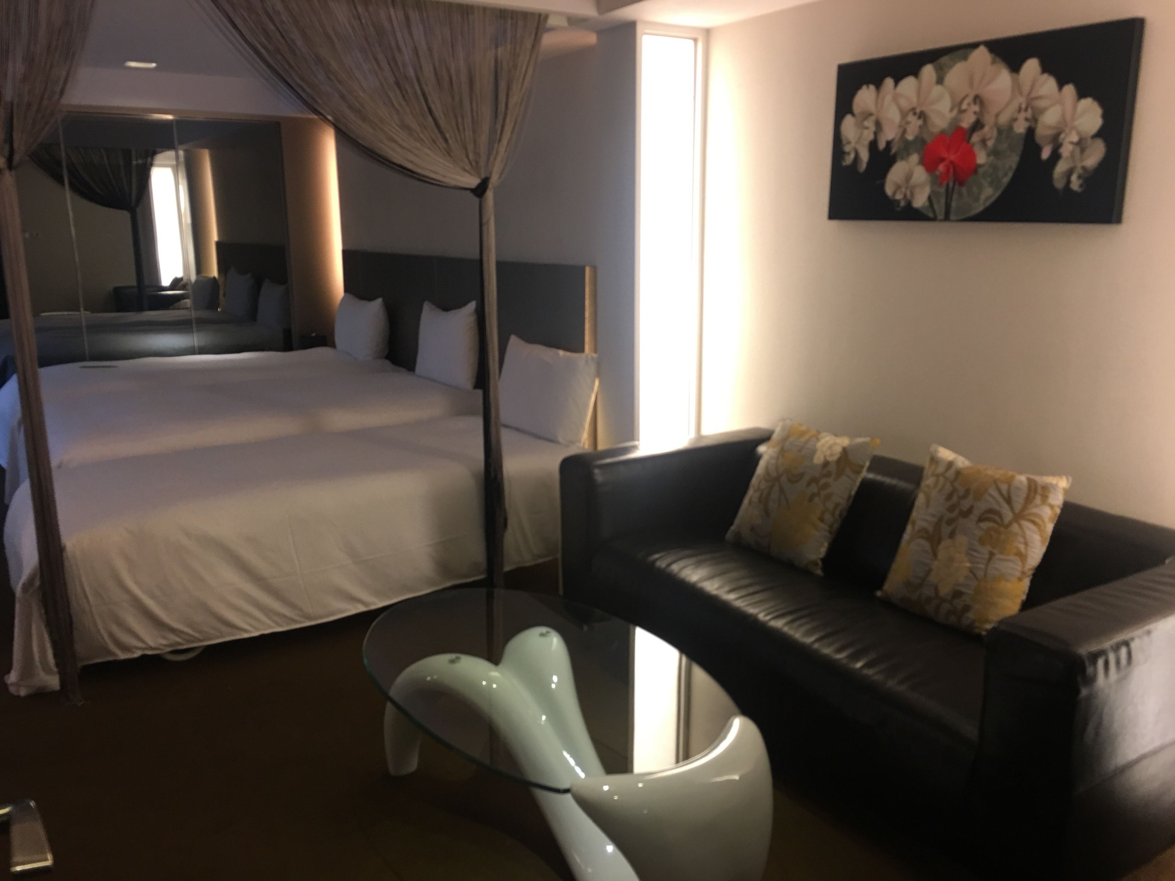 Una habitación de hotel con una cama grande, un sofá de cuero negro, una mesa de centro de vidrio y un cuadro en la pared.