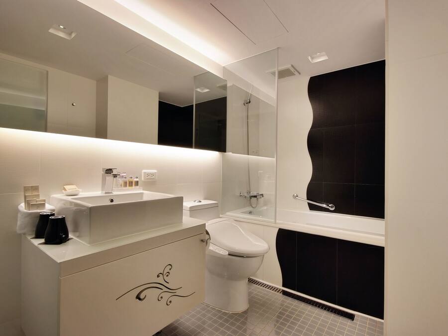 A modern bathroom with a white vanity, a toilet, a bathtub, and a large mirror.