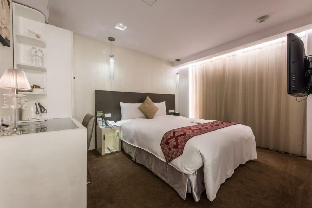 Een hotelkamer met een bed, een televisie, een nachtkastje, een lamp en een kledingkast.