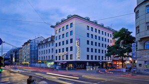 Un hotel de varios pisos con un letrero llamativo, situado en una concurrida intersección urbana.
