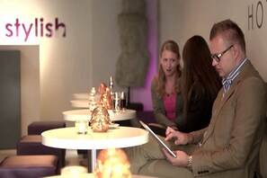 A modern interior with round tables and chairs, a 'stylish' sign on the wall, and a person holding a tablet. - Rilano 24 - 7 Hotel Munchen City (Munich)