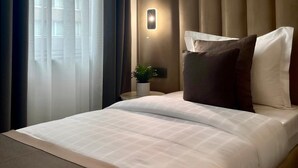 Una habitación de hotel con una cama grande, una mesita de noche con lámpara y cortinas traslúcidas.