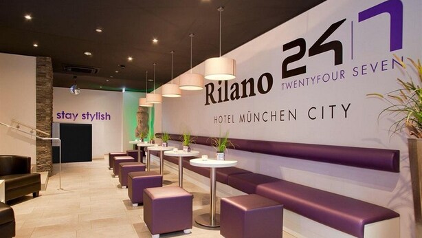 Un moderno vestíbulo de hotel con un gran letrero que dice "Rilano 24/7 HOTEL MÜNCHEN CITY".