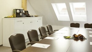 Un salón de conferencias con una larga mesa, seis sillas, una estación de café y dos tragaluces.