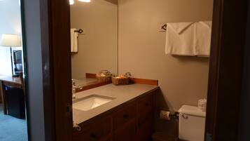 A bathroom with a sink, mirror, and toilet. There are baskets on the sink counter and a towel hanging on the wall.