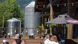 An outdoor seating area with wooden tables and chairs, a large metal water tank, and a building with a wooden facade.