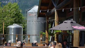 An outdoor seating area with wooden tables and chairs, a large metal water tank, and a building with a wooden facade.
