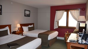 A hotel room with two beds, a desk with a chair, a lamp, and a window with curtains.