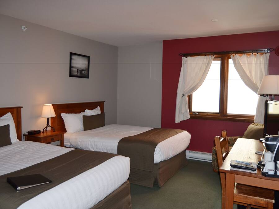 A hotel room with two beds, a desk with a chair, a lamp, and a window with curtains.