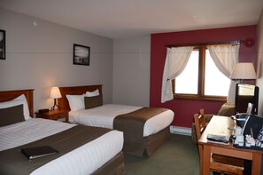 A hotel room with two beds, a desk with a chair, a lamp, and a window with curtains.