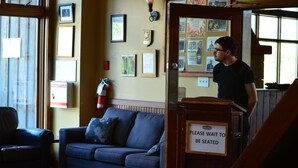 A waiting area with a blue sofa, a fire safety plan sign, and a "Please wait to be seated" sign.