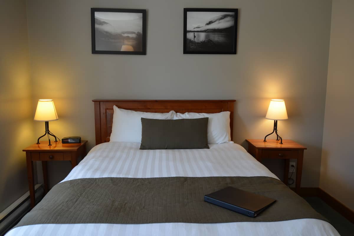 A neatly made bed with a gray blanket, two bedside lamps, and a laptop on the bed.