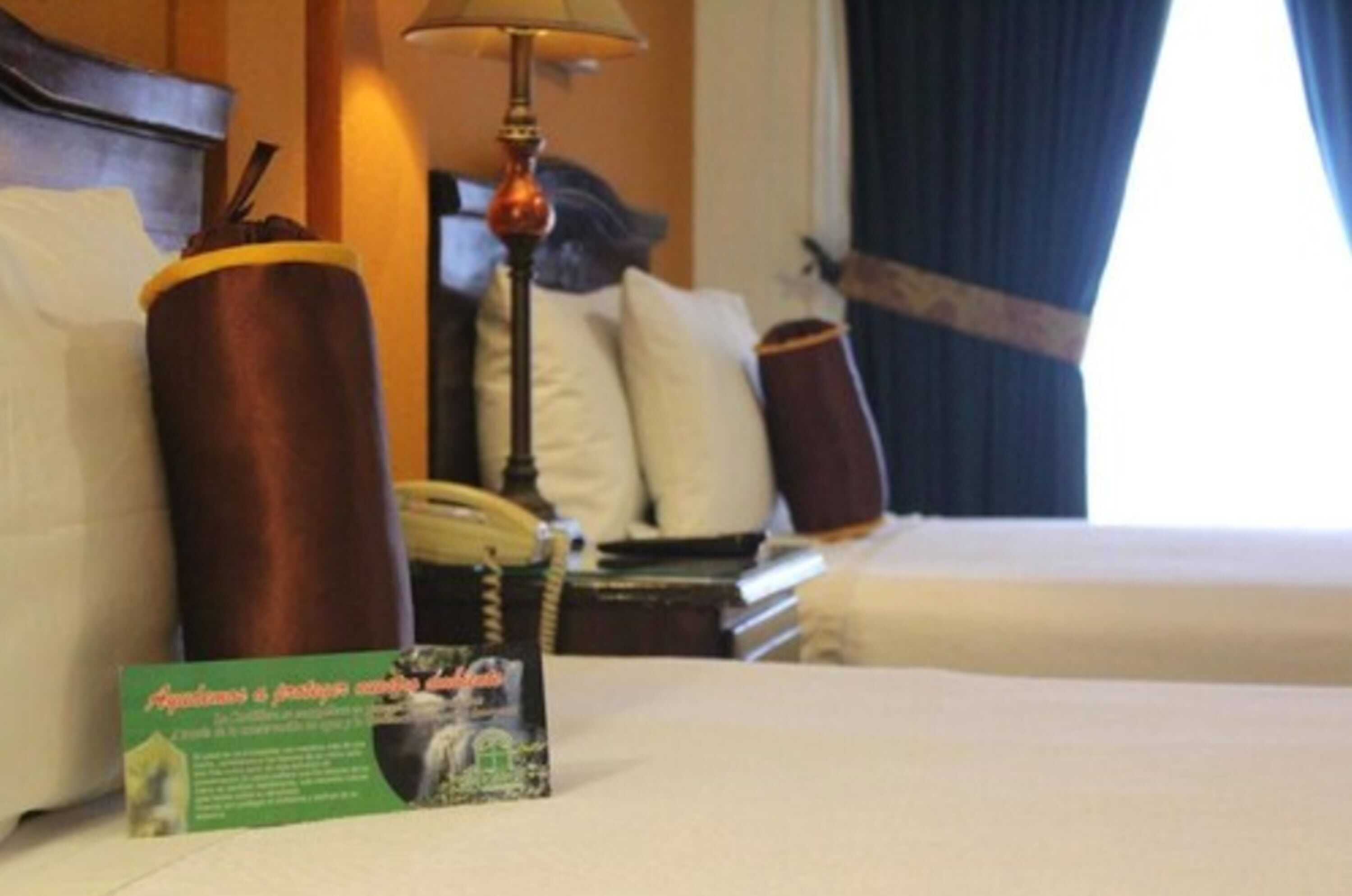 A hotel room with a bed, a lamp, a telephone, and a brochure on the bed.