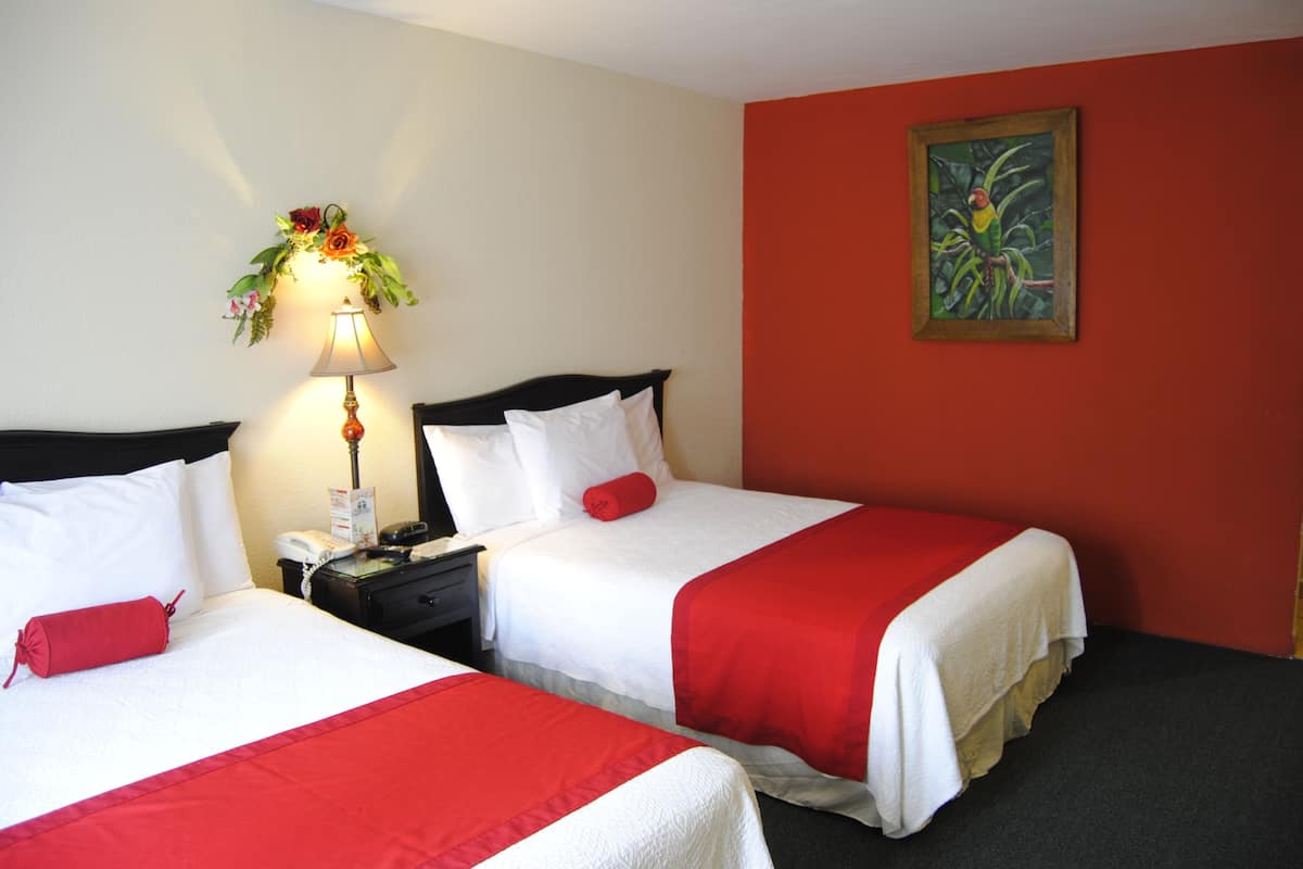 A hotel room with two beds, a nightstand, a lamp, a telephone, and a painting on the wall.