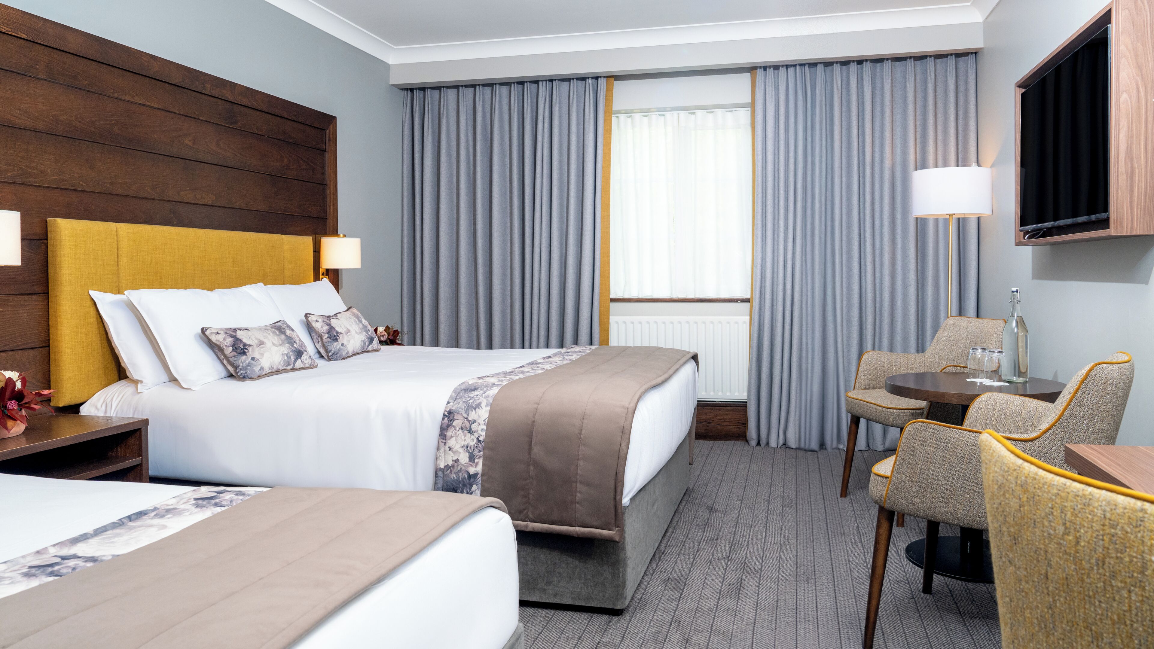 A hotel room with a bed, a desk, a chair, a TV, and a window with curtains.