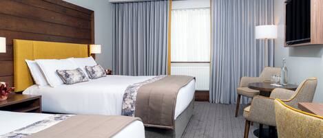 Habitación de hotel con cama, escritorio, silla, televisor y ventana con cortinas.