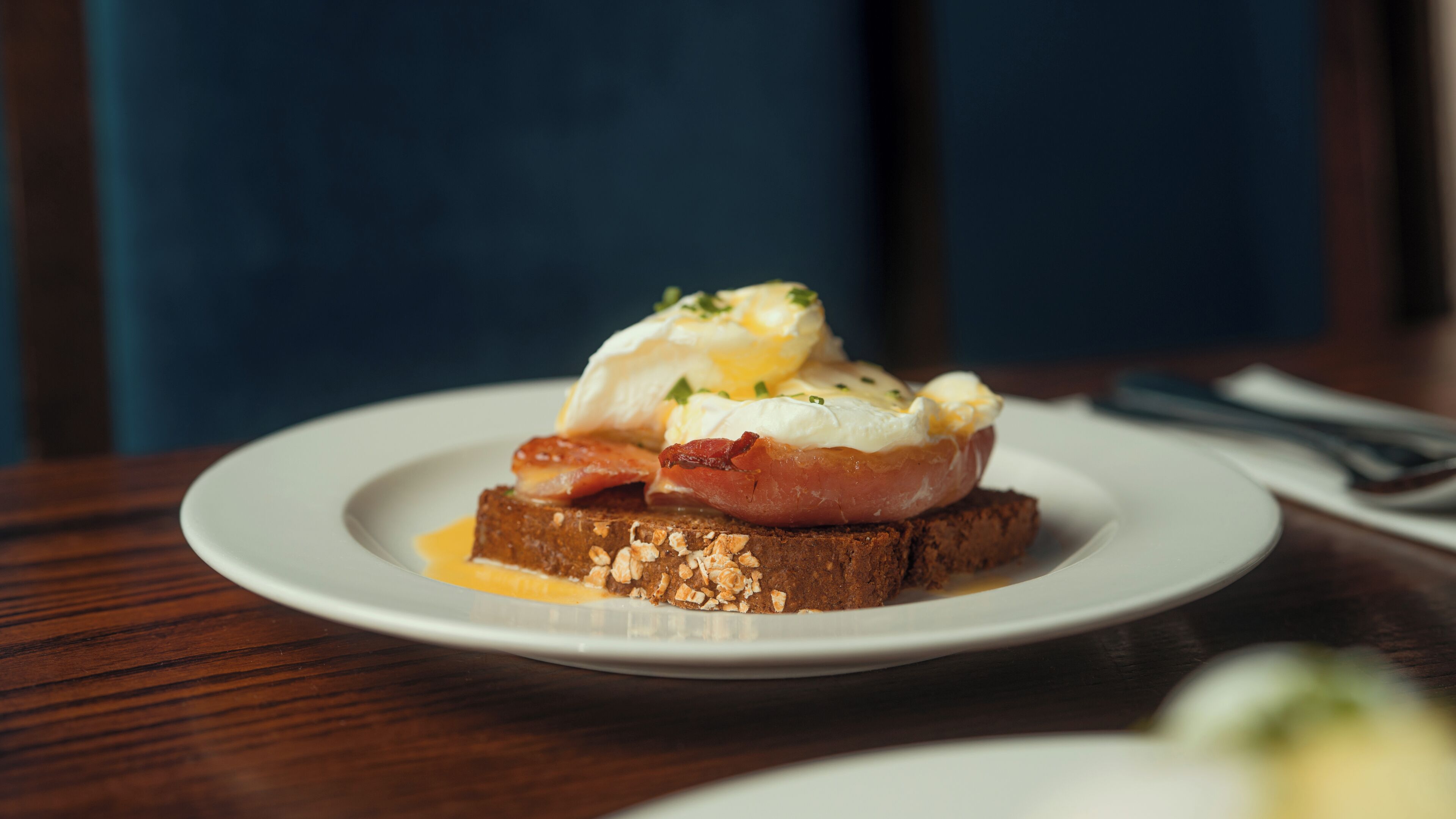 A plate with a breakfast dish consisting of eggs, bacon, and toast on a wooden table.