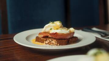 A plate with a breakfast dish consisting of eggs, bacon, and toast on a wooden table.