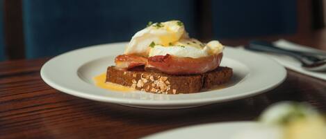 A plate with a breakfast dish consisting of eggs, bacon, and toast on a wooden table.
