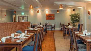 Un restaurante con mesas y sillas de madera, un banco acolchado, lámparas colgantes y un cuadro en la pared.