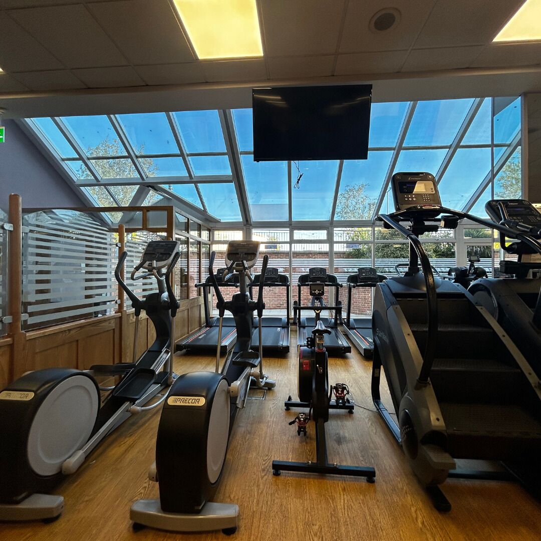 A gym with various cardio machines, a large window with a view of the outdoors, and a mounted television.