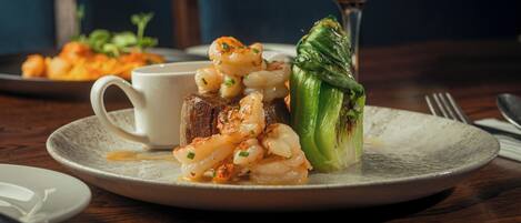 A plate with grilled shrimp, a piece of meat, and a stuffed vegetable, accompanied by a glass of red wine.