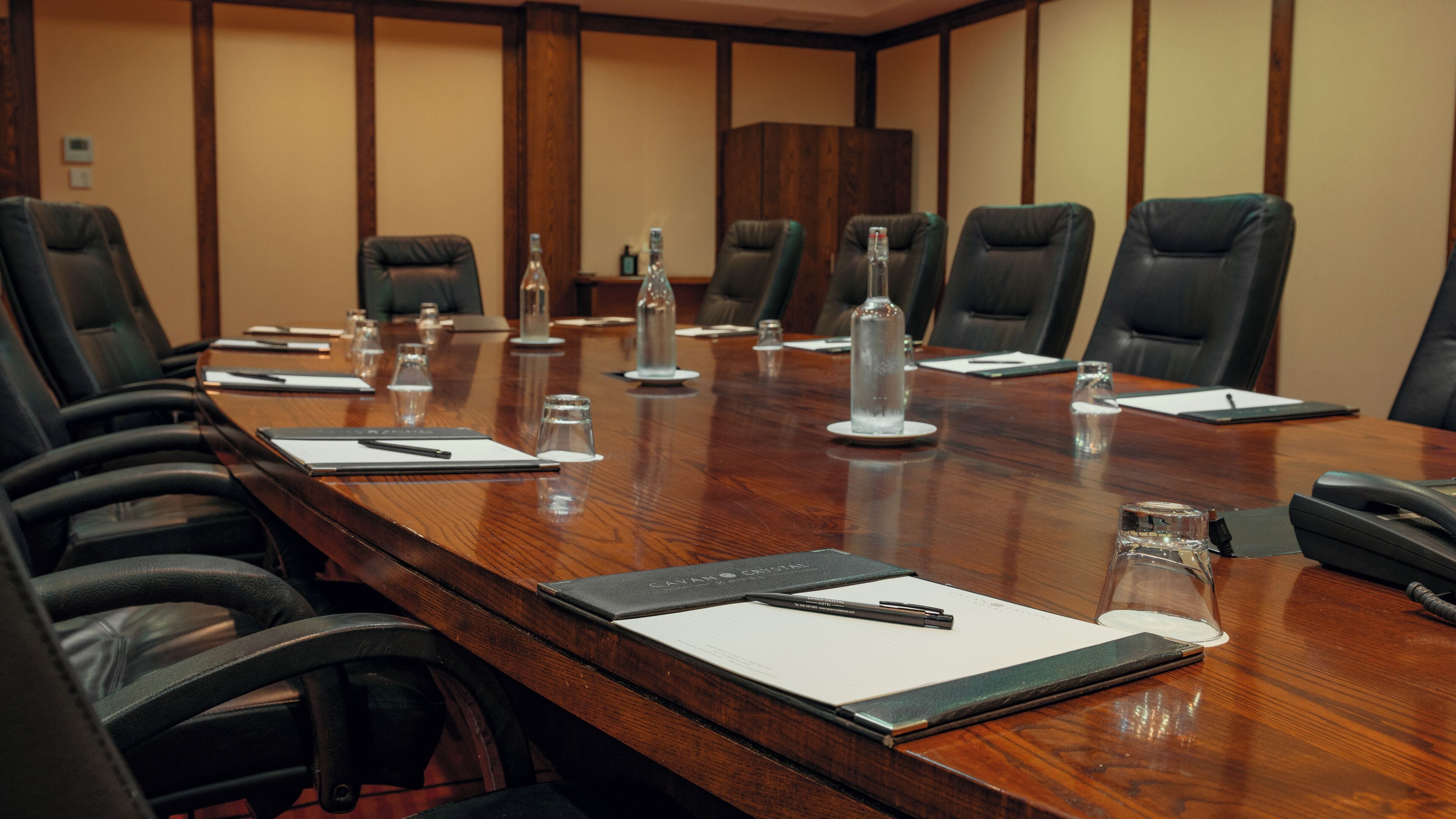 A conference room with a long wooden table, black leather chairs, water bottles, and nameplates.
