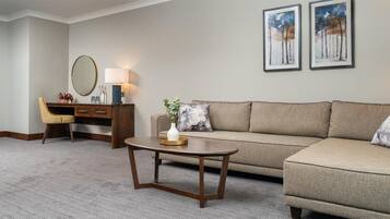 A living room with a sofa, a coffee table, a desk with a chair, a lamp, and two framed pictures on the wall.