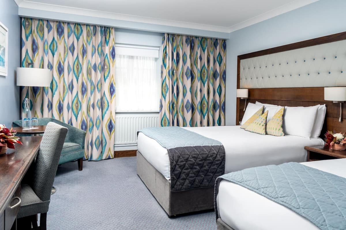 A hotel room with two beds, a desk, and a chair.